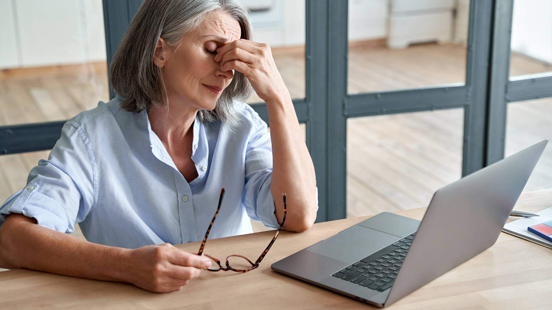 Overworked and stressed mature senior business woman suffering from fatigue, headache, having eyesight problem after computer work. Overwork and stress can contribute to diseases like osteoporosis.