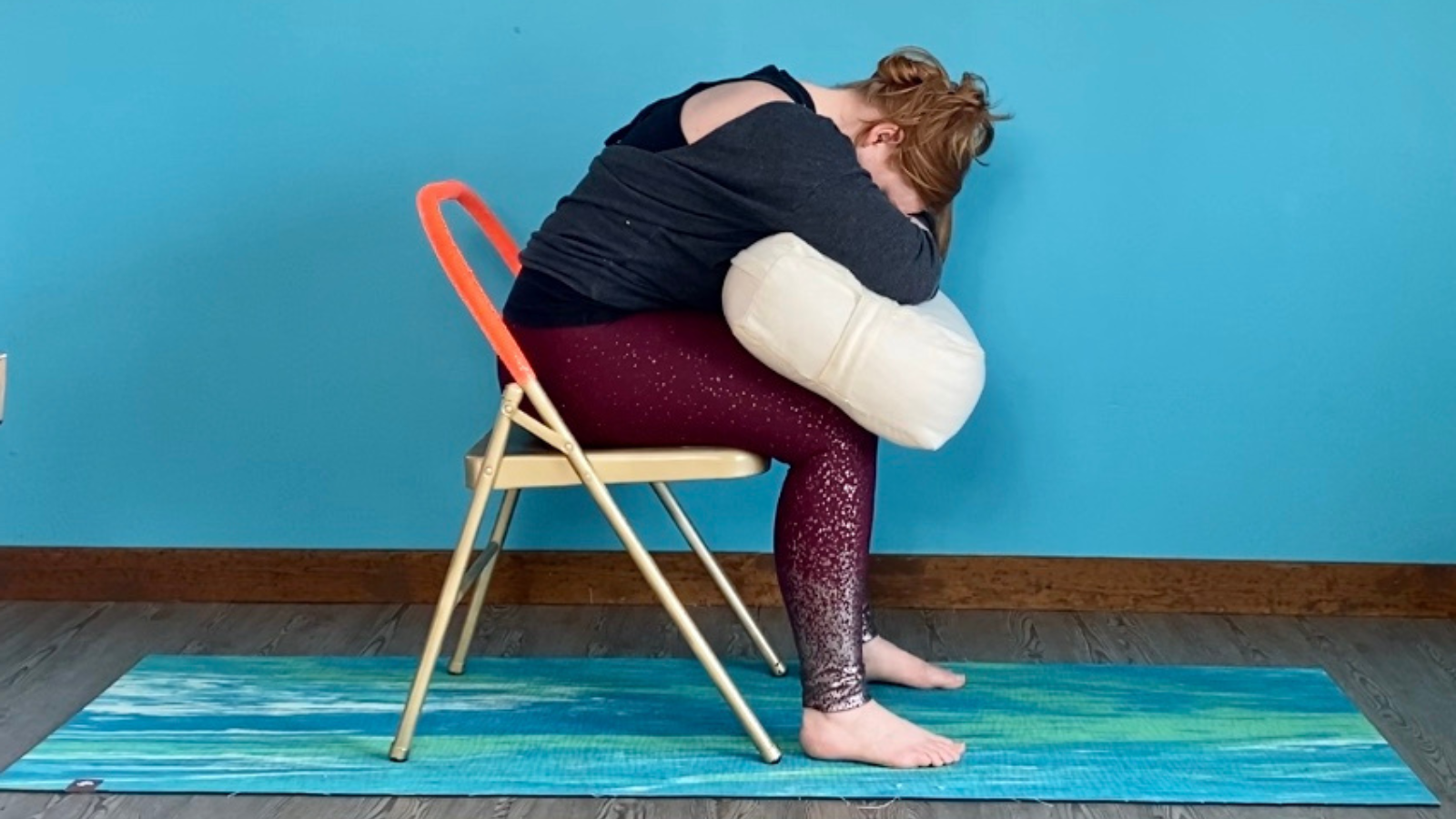 A Restorative Forward Fold Child's Pose or Balasana practiced in a chair with a bolster for support. 