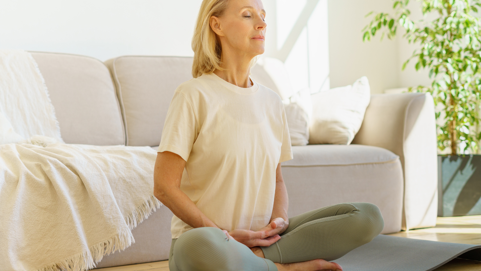 Peaceful senior woman in lotus position meditation with closed eyes at home practicing yoga.