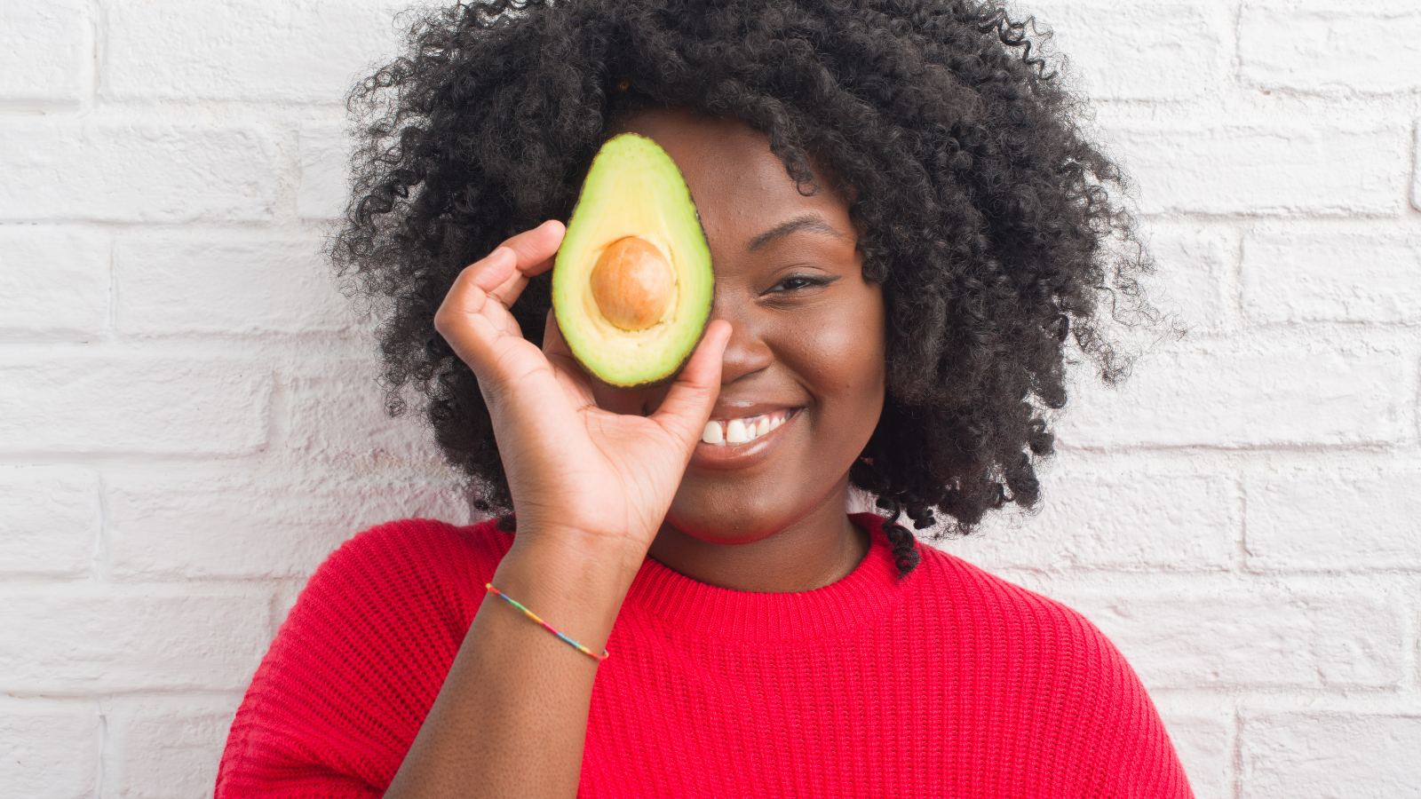 Young african american woman over white brick wall eating heart-healthy avocado