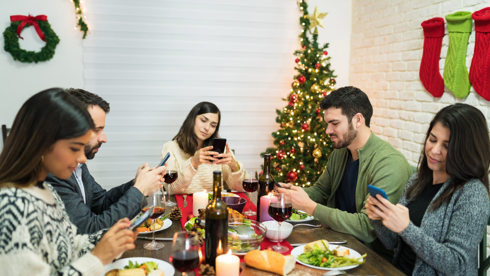 Distracted friends using smartphones while having meal at dining table during Christmas celebrations at home