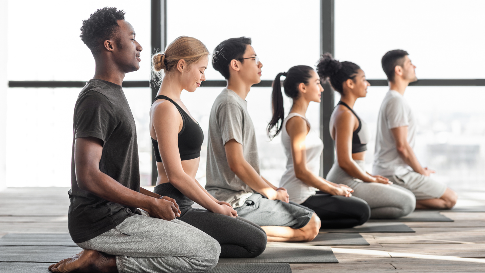 multiracial men and woman practicing yoga and meditating together in modern studio in celebration of International Yoga Day