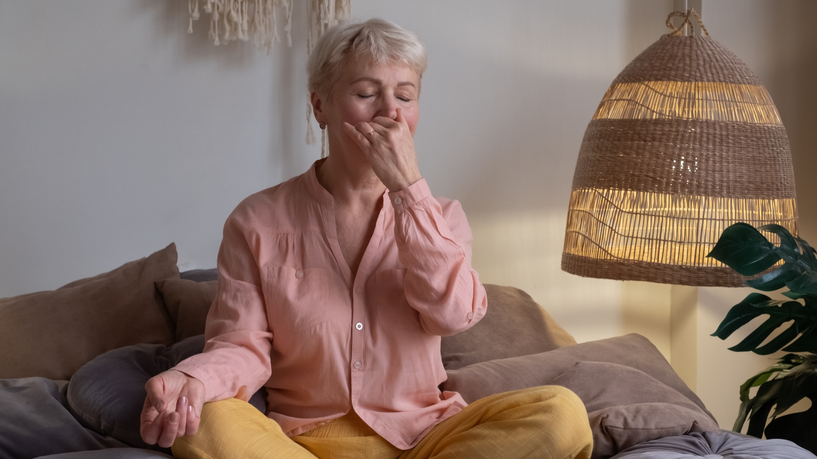 Senior woman practicing yoga at home, making Alternate Nostril Breathing or, nadi shodhana pranayama as a practice to reduce the risk of heart conditions such as atrial fibrillation.