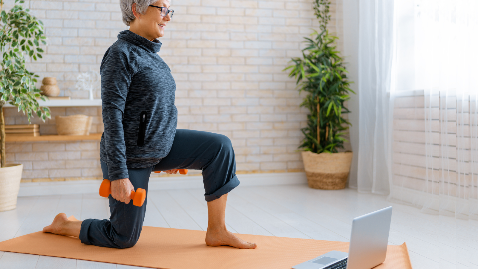Senior woman in activewear watching online courses on laptop while exercising at home.