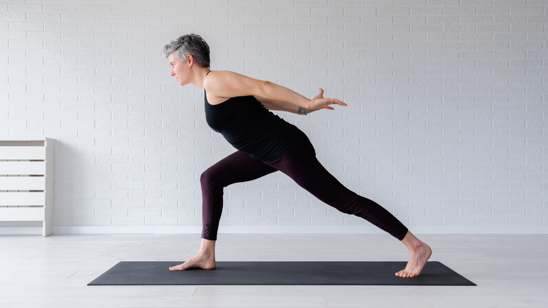 A senior woman practicing Virabhadrasana I (Warrior I Pose) to increase strength and flexibily and reduce muscle imbalances.