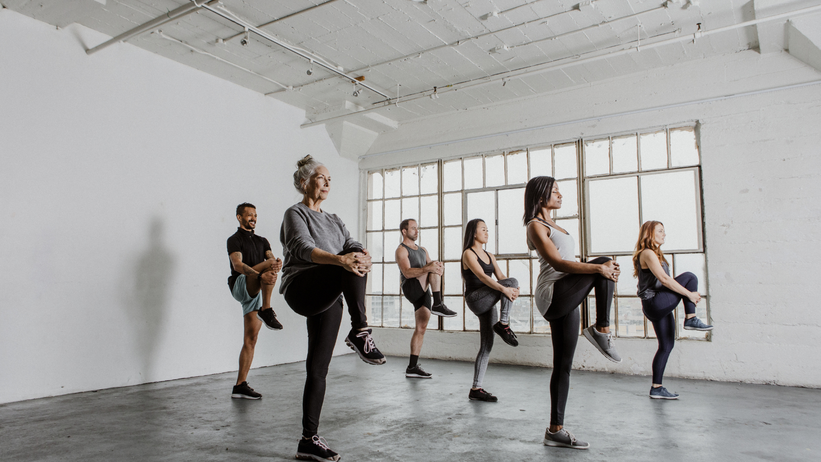  older woman among diverse people stretching their knees and practicing balance in a yoga class to help relieve arthritis pain