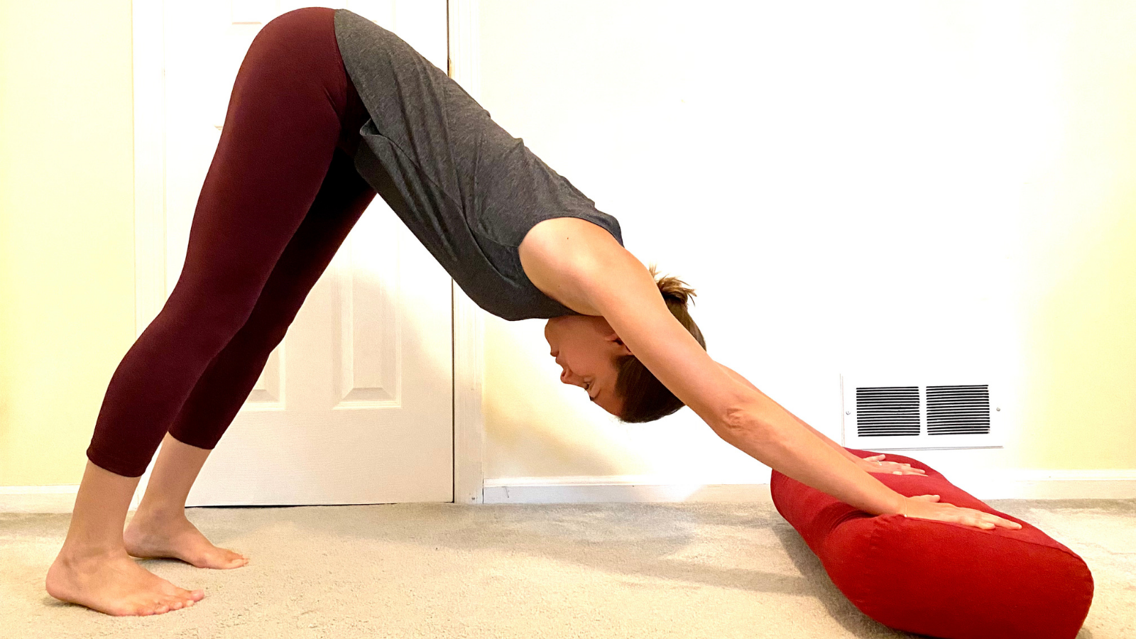 Variation of Down Dog (Adho Mukha Svanasana) adding a bolster under the hands to create more comfort and space