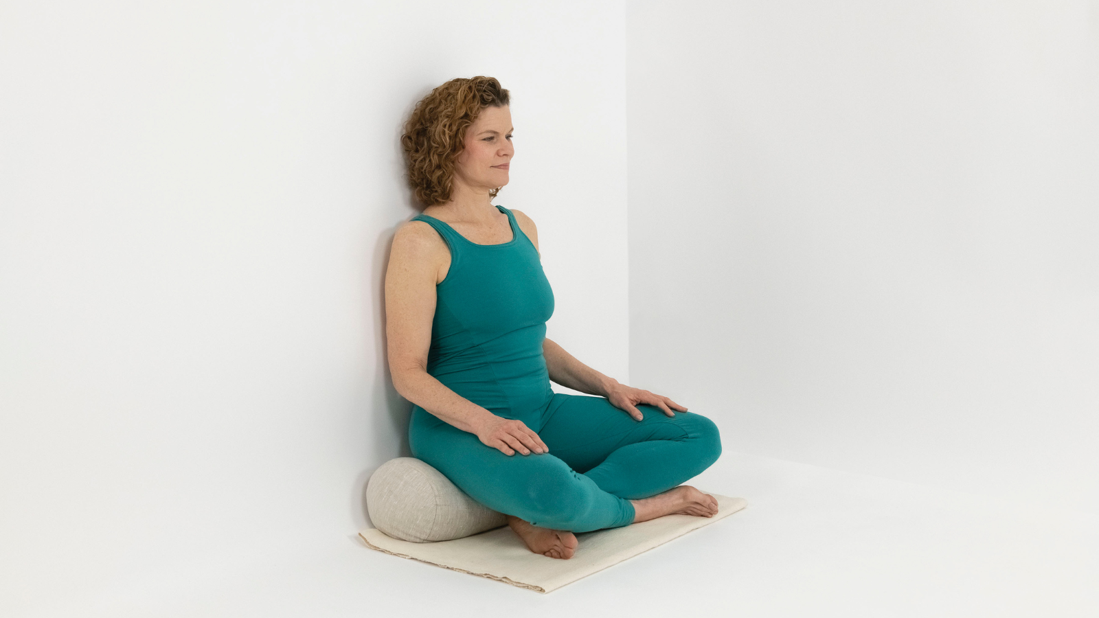 Supported Easy Sitting Pose or Sukhasana with the extra restorative support of the wall, blanket and bolster