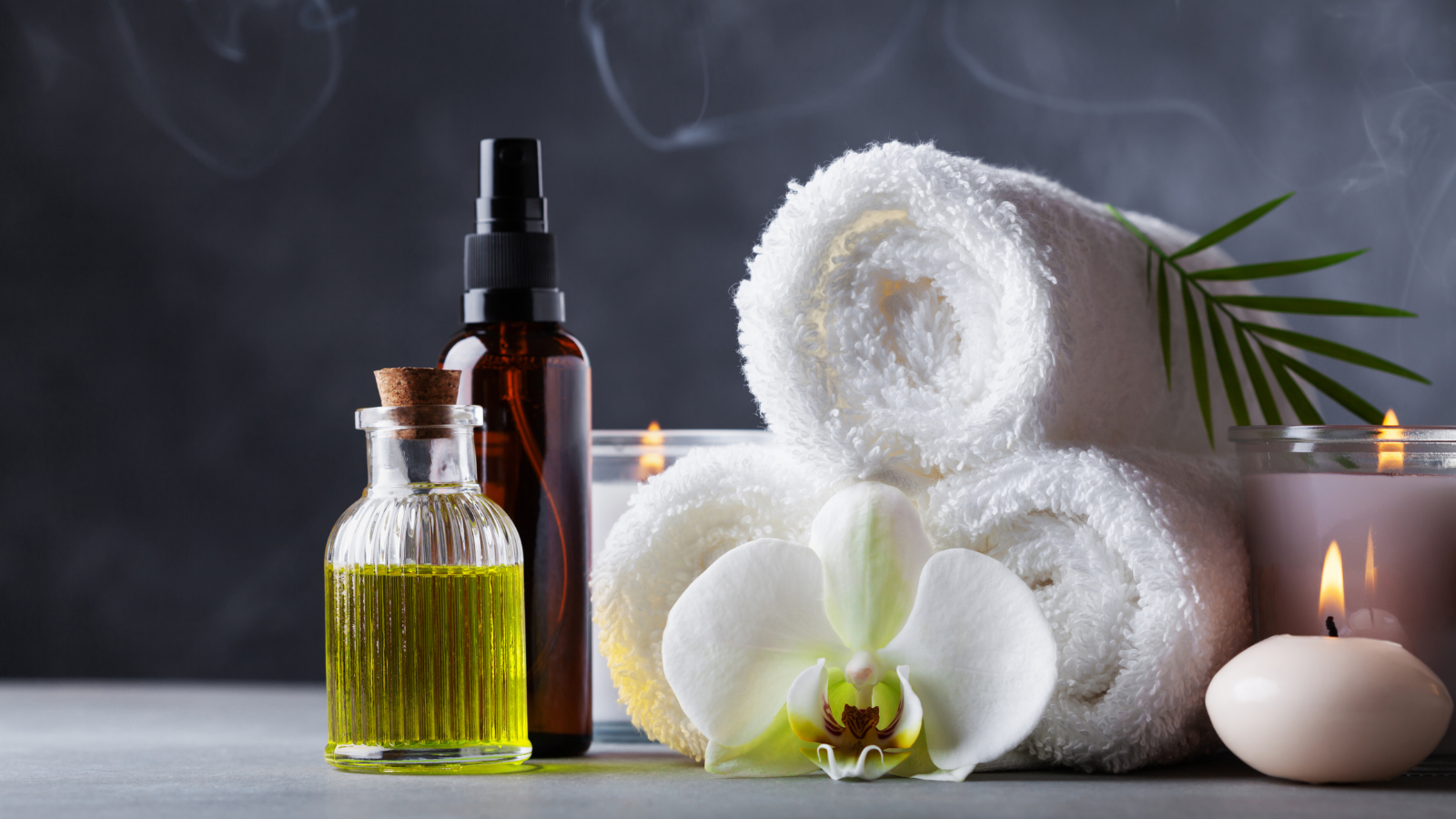 Aromatherapy, spa, beauty treatment and wellness background with massage oil, orchid flowers, towels, and candles.