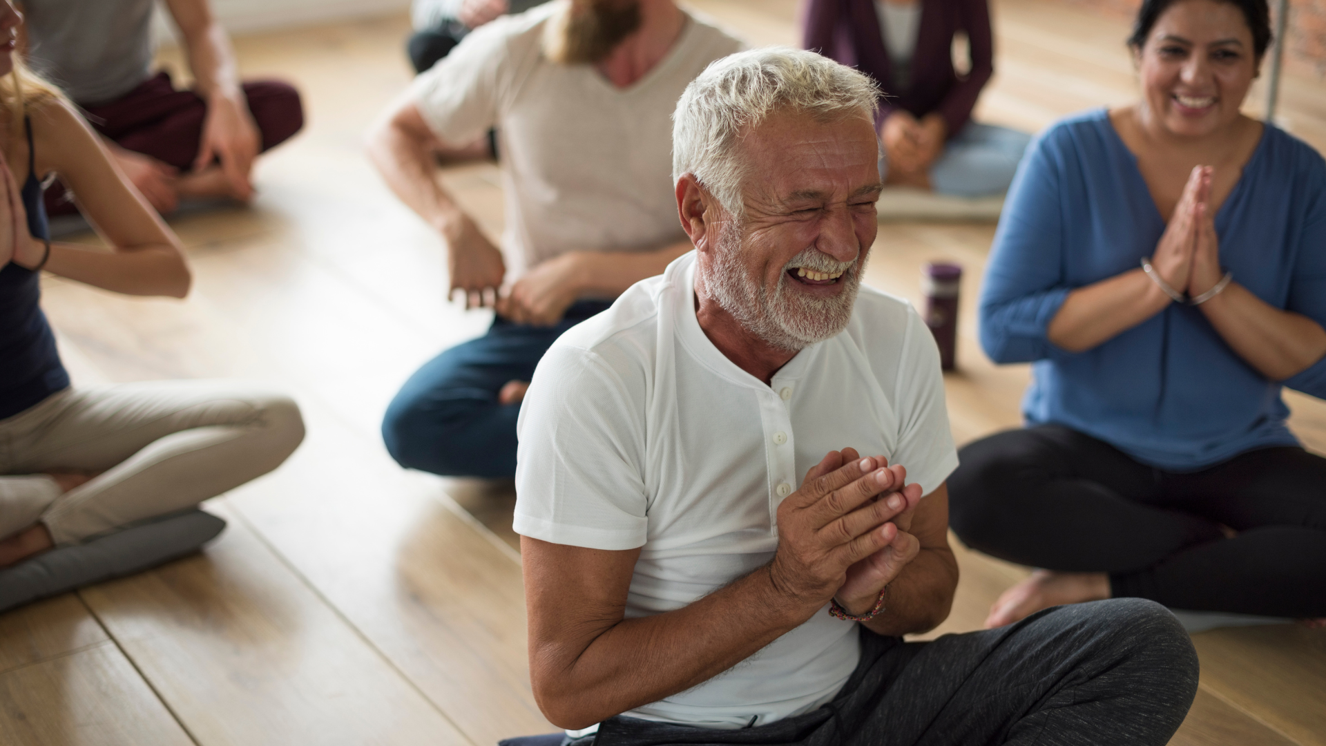 An elderly man laughs with his hands at heart center in a yoga practice to reduce inflammatory biomarkers
