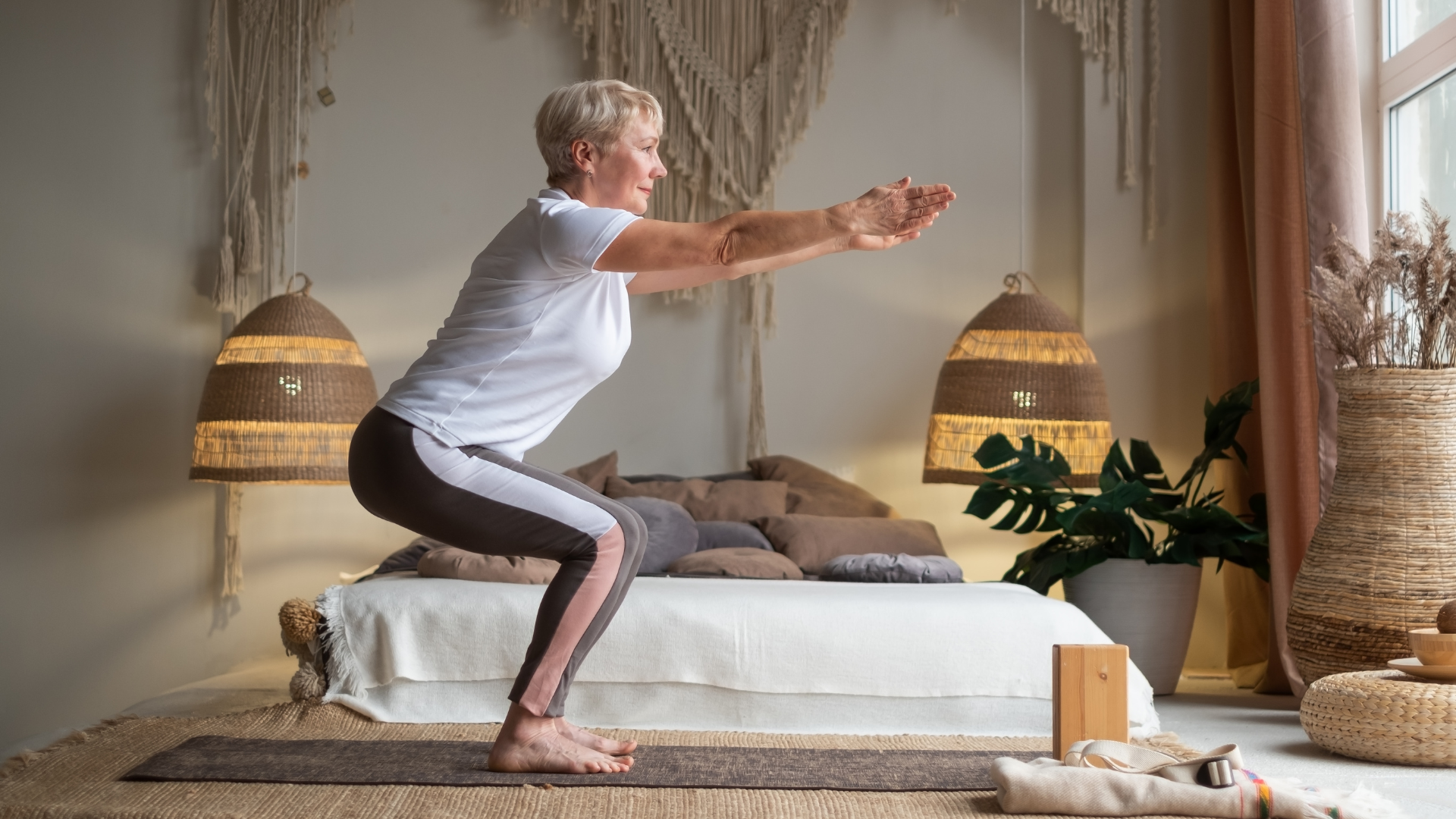 Senior woman practicing advanced yoga Chair Pose Utkatasana at home