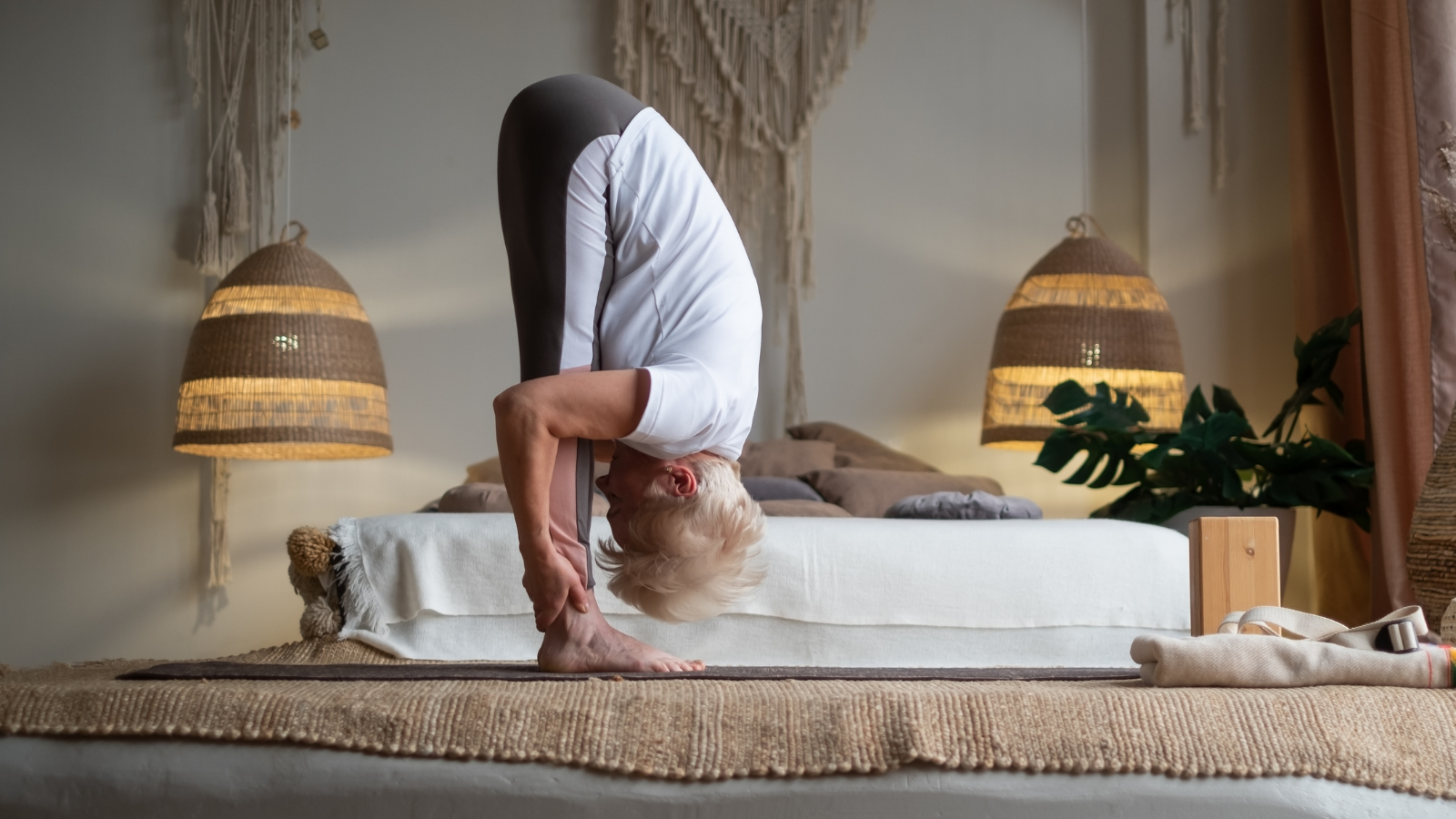Senior woman working out practicing Standing Forward Bend or Uttanasana at home