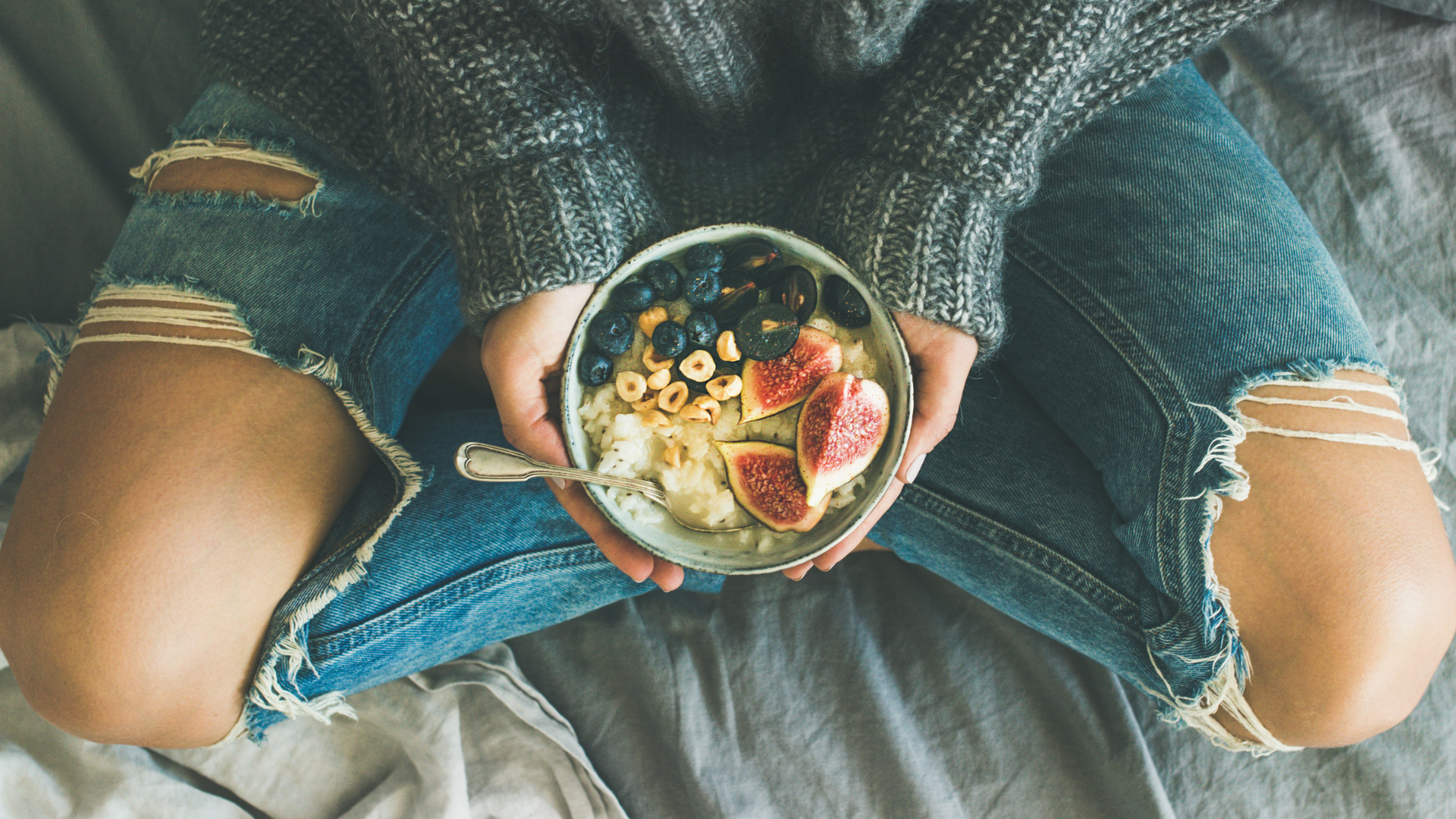 Healthy winter breakfast. Woman in sweater and jeans holding rice porridge with figs, berries, hazelnuts. Clean eating concept for healthy muscles and bones.