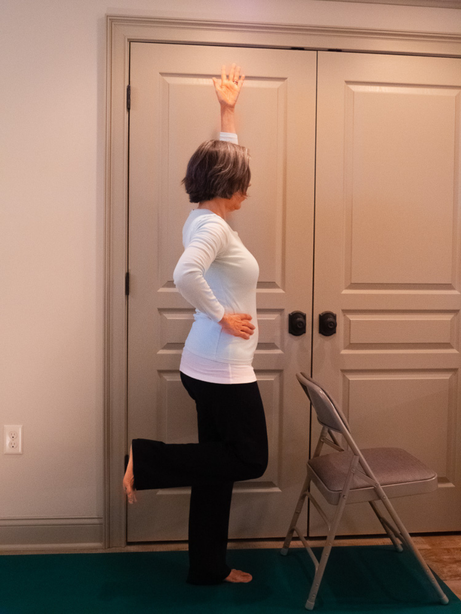 Dancer's Pose or Natarajasana, a beginner-friendly balance pose, is shown in a variation with one arm raised high.